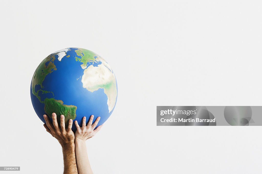 Two people holding globe in raised hands against white background,close-up