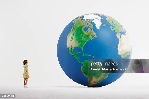 girl (8-9) standing in empty white room, looking at huge globe (digital enhancement) - american girl alone stock-fotos und bilder