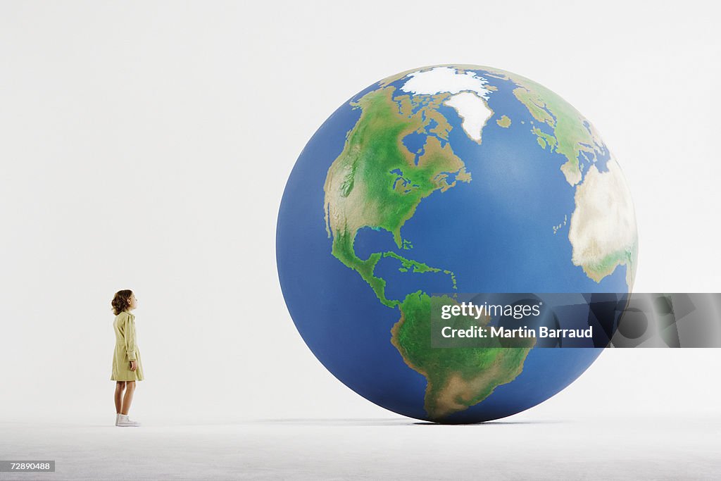 Girl (8-9) standing in empty white room, looking at huge globe (digital enhancement)