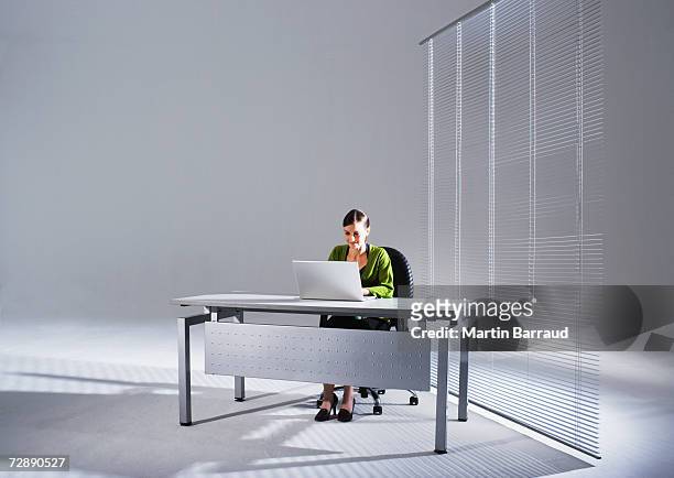 young businesswoman sitting at desk, using laptop - scrivania foto e immagini stock