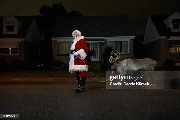 father christmas standing in road with reindeer, side view - santa stock-fotos und bilder