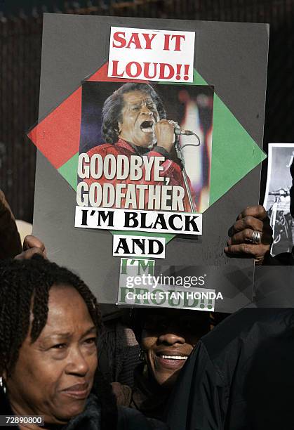 New York, UNITED STATES: A woman holds a sign with the title of one of the more famous James Brown songs as people wait in line outside the Apollo...