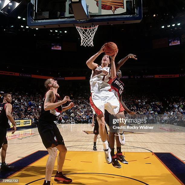 Troy Murphy of the Golden State Warriors takes the ball to the basket against Joel Przybilla and Zach Randolph of the Portland Trail Blazers during a...