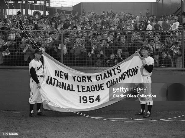 Alvin Dark and Whitey Lockman hold up the 1954 pennant prior to the Opening Day game on April 14, 1955 against the Brooklyn Dodgers at the Polo...