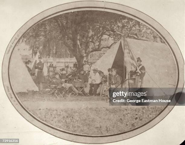 View of group of uniformed Union soliders as they sit outside tents in a military camp, 1860s. A figure who resembles American President Abraham...