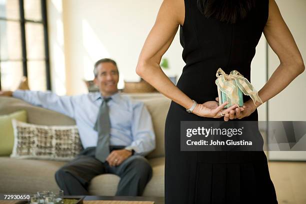 couple in living room, woman hiding gift behind back - se cacher photos et images de collection