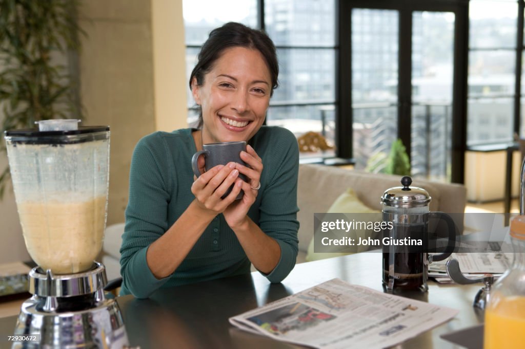 Woman holding mug by blender on kitchen counter, portrait
