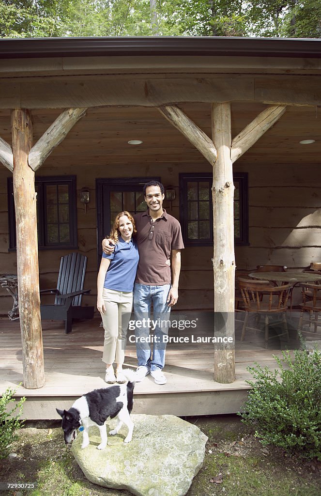 Young couple standing on porch with dog, smiling, portrait