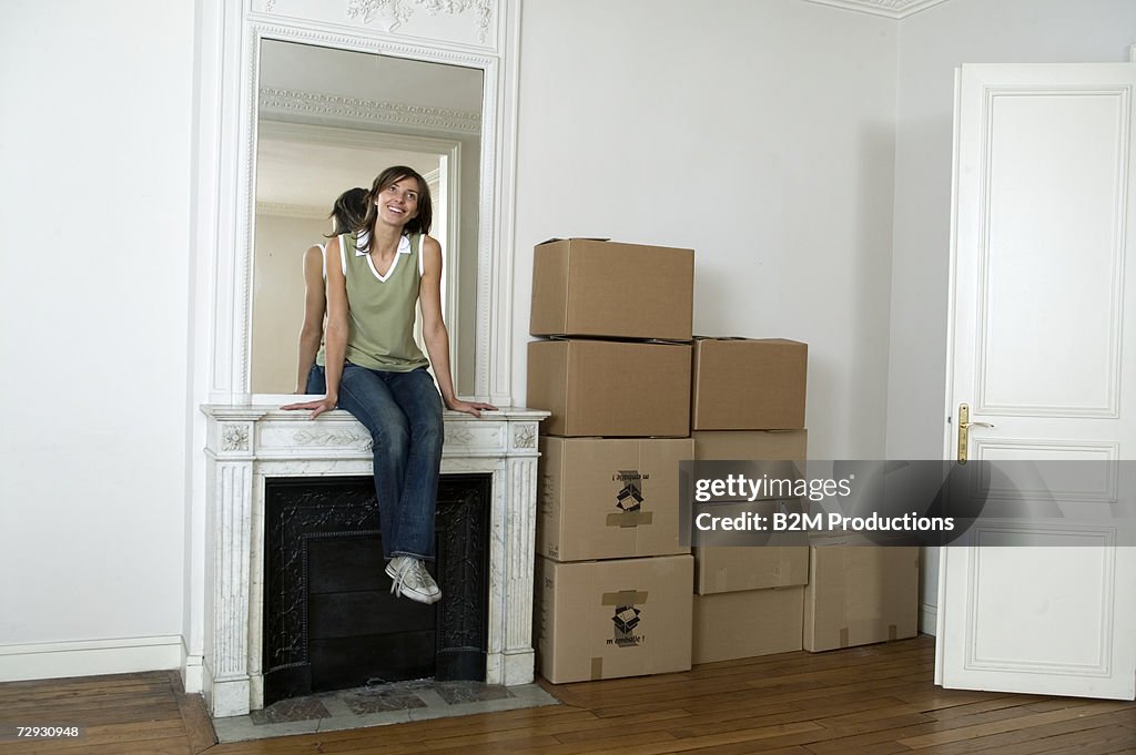 Young woman sitting on mantelpiece, beside packing boxes