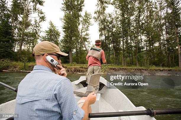 young man using cell phone while fly-fishing on the elk river from a dory, fernie, east kootenays, british columbia, canada. - bc commercial fishing boats stock pictures, royalty-free photos & images