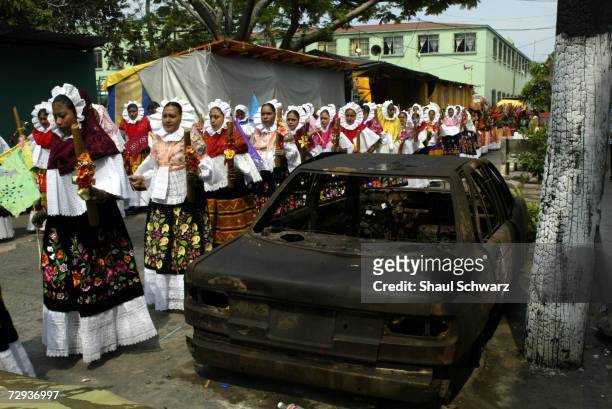 Women parade in the street past a burned out car during a Regada Ceremony in Juchitan, Mexico, June 5, 2003. Whether it is a religious ceremony or an...