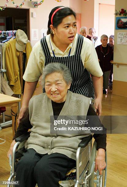 Olivia Pineda from the outskirts of Manilla, Philippines, supports a Japanese elderly woman to move her wheelchair prior to a year-end party in a...