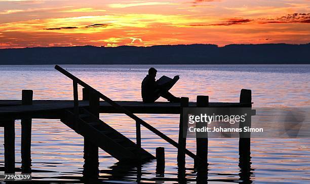 Man sits on a dock reading a newspaper at the beach of Ammersee Lake the mild winter evening on January 10, 2007 in Herrsching, Germany. Bavaria and...