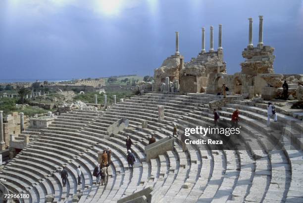 Tourists walk up steps of the theater's tiered seating area , which provides views of the expansive city ruins of Leptis Magna, the largest city of...