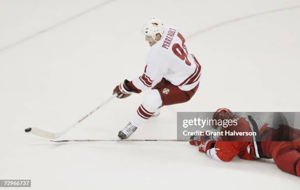 Yanic Perreault of the Phoenix Coyotes plays the puck as Glen Wesley of the Carolina Hurricanes slides on the ice to defend during the NHL game on...