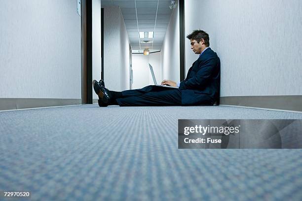 businessman in a hallway working on a laptop computer - profile laptop sitting stock-fotos und bilder