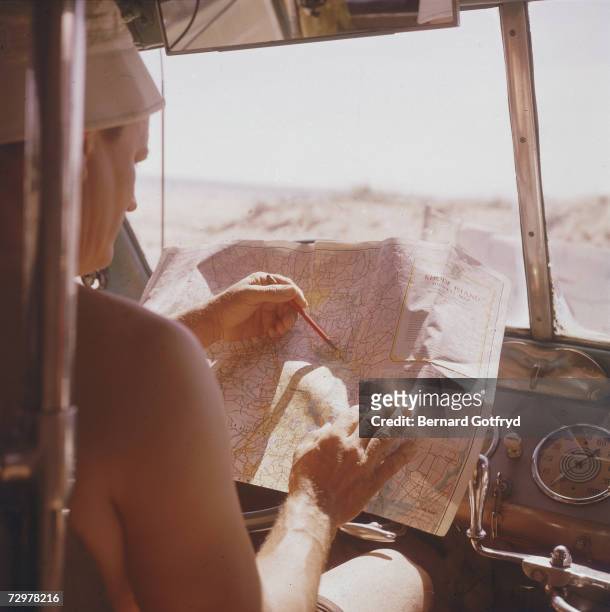 An unidentified shirtless man sits in the driver's seat of a bus and plots a course through Rhode Island on a map, 1950s.