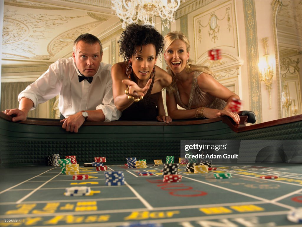 Woman throwing dice at craps table in casino, friends watching