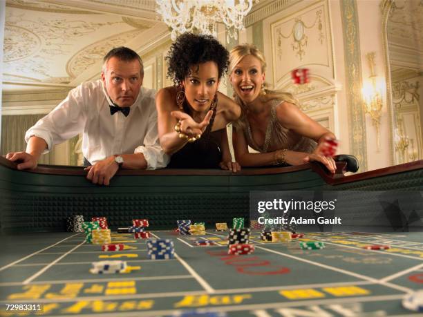 woman throwing dice at craps table in casino, friends watching - casino dice stock pictures, royalty-free photos & images