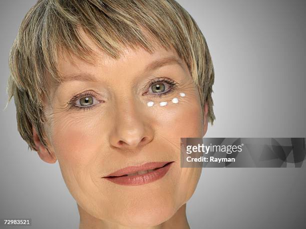 mature woman with skin cream under eye, close-up - aging skin stock-fotos und bilder