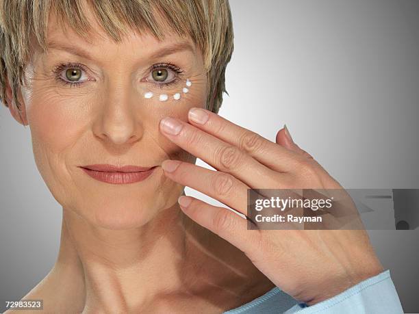 mature woman rubbing skin cream on face, portrait - aging skin stock-fotos und bilder