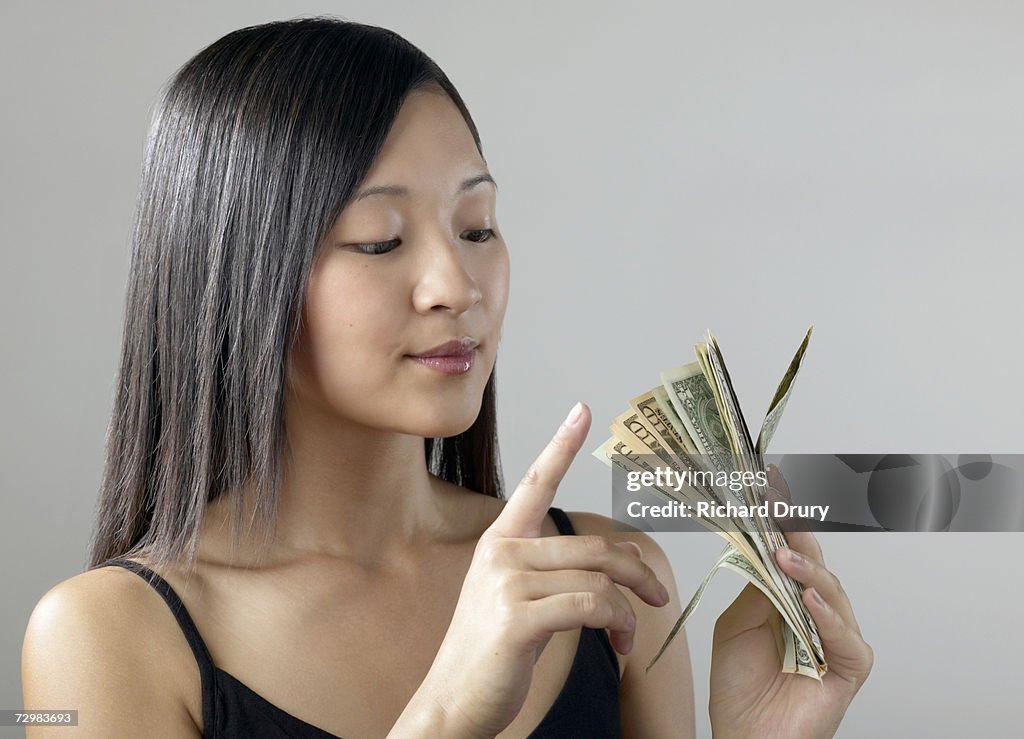 Young woman holding wad of dollar bills, counting the money