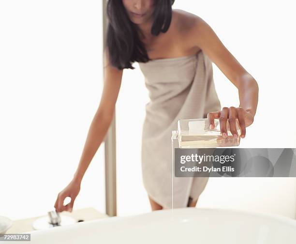 young woman wrapped in towel pouring bath oil into bath, low section - apothecary bottle stock pictures, royalty-free photos & images