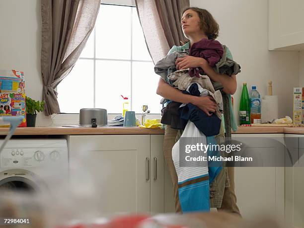 "woman in kitchen holding laundry, looking careworn" - trabalho fastidioso - fotografias e filmes do acervo