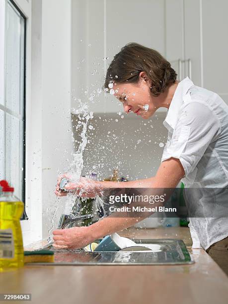 woman at sink in domestic kitchen being drenched by broken tap, side view - drenched stock pictures, royalty-free photos & images