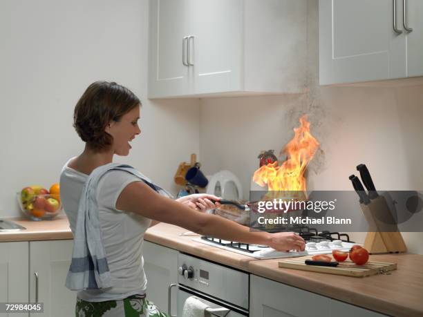 woman with anguished expression holding burning frying pan in domestic kitchen - burning stock pictures, royalty-free photos & images