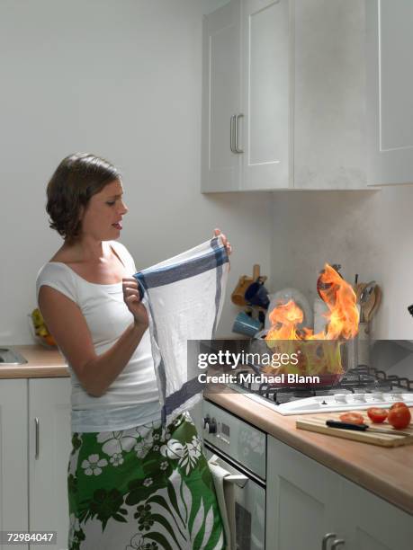 woman with tea towel attempting to extinguish burning pan in domestic kitchen - extinguishing stock pictures, royalty-free photos & images