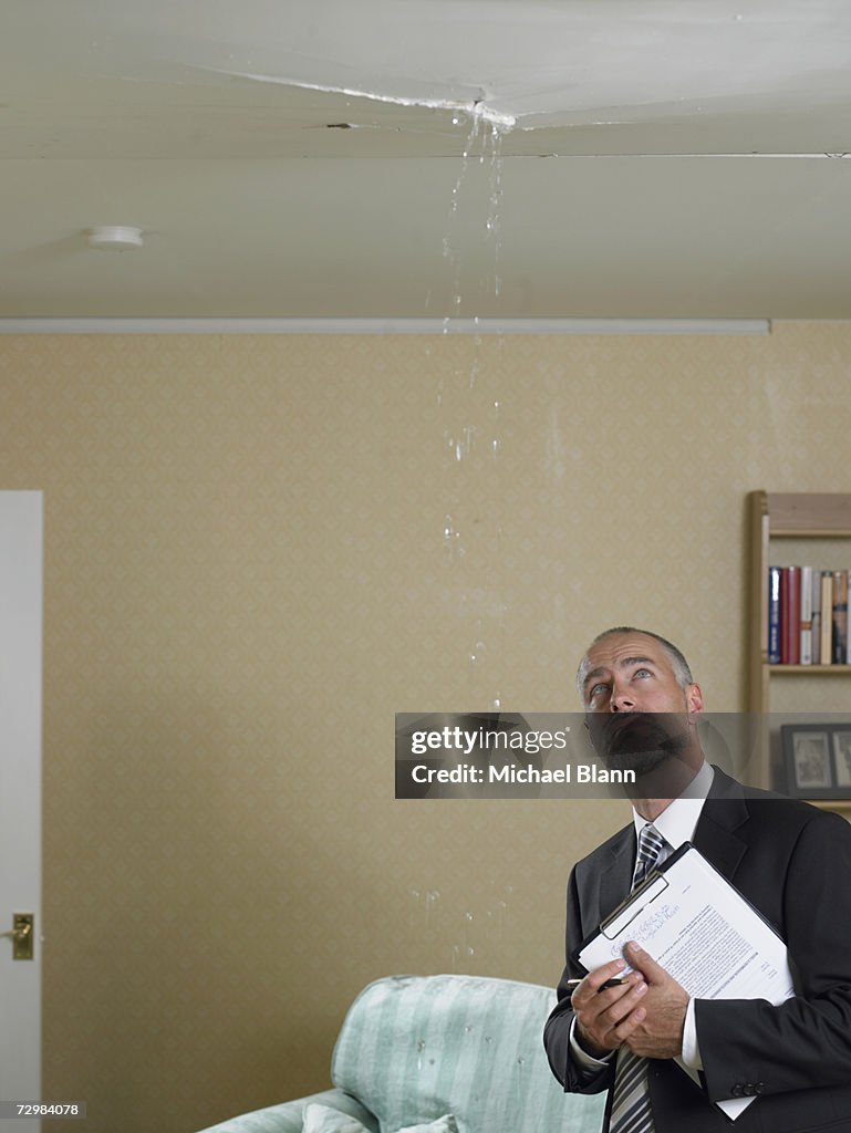 Mature man in suit with clipboard looking at water dripping from crack in ceiling
