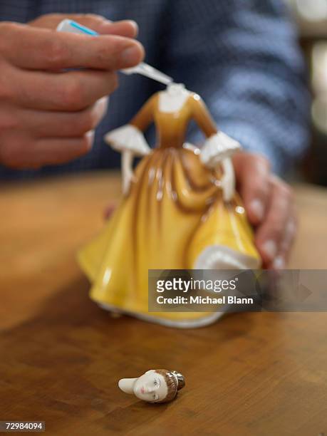 mature man applying glue to neck of broken china figurine - broken figurine stock pictures, royalty-free photos & images