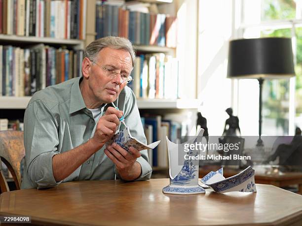 mature man sitting at table repairing broken china vase - broken vase stock pictures, royalty-free photos & images