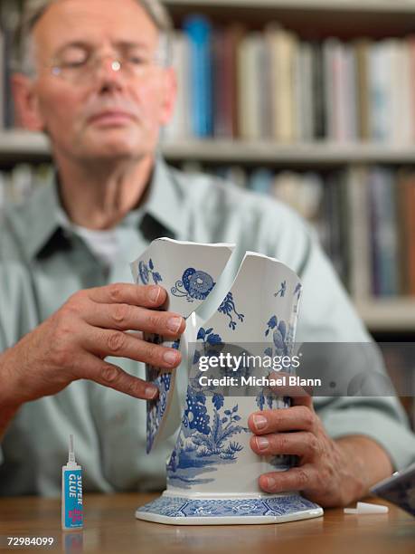 mature man sitting at table repairing broken china vase - broken finger ストックフォトと画像