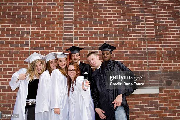 teenage male and female graduates (16-19) wearing graduation caps and gown, taking self portrait - male student wearing glasses with friends stock-fotos und bilder