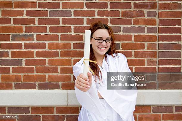 young woman wearing graduation clothing, holding diploma, smiling - college graduate diploma stock pictures, royalty-free photos & images