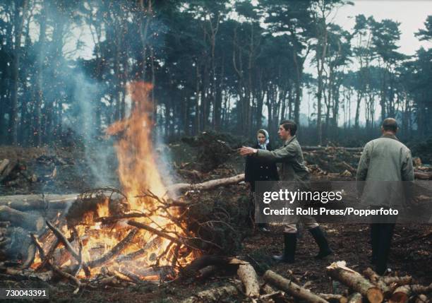 Prince Charles pictured placing branches on a bonfire as his sister Princess Anne looks on and his father Prince Philip, Duke of Edinburgh walks off...