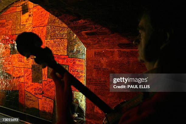 Liverpool, UNITED KINGDOM: A man plays the mandolin in front a wall of names in the Cavern Club in Liverpool, north-west England, 16 January 2007....