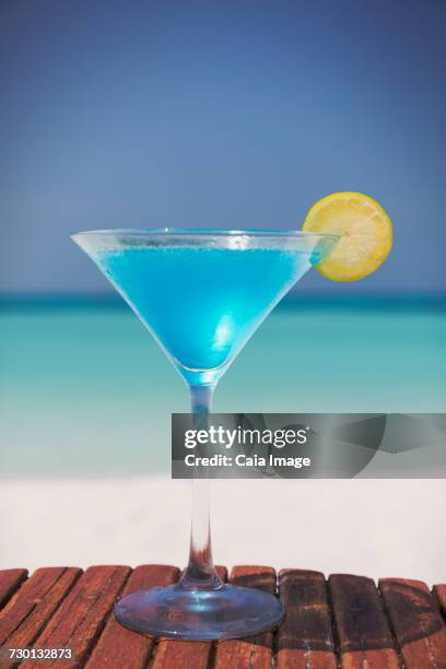 blue cocktail with lemon slice in martini glass on sunny tropical beach - blue martini glasses stock-fotos und bilder