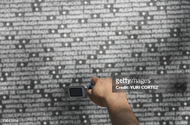 San Salvador, EL SALVADOR: Un hombre toma una fotografia, con su telefono celular, del nombre de su pariente estampado en un mural con los de miles...