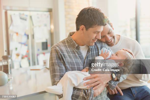 Affectionate male gay parents holding baby son with bottle