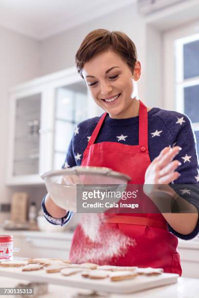smiling woman baking, sifting sugar over cookies in kitchen - powdered sugar sifter fotografías e imágenes de stock