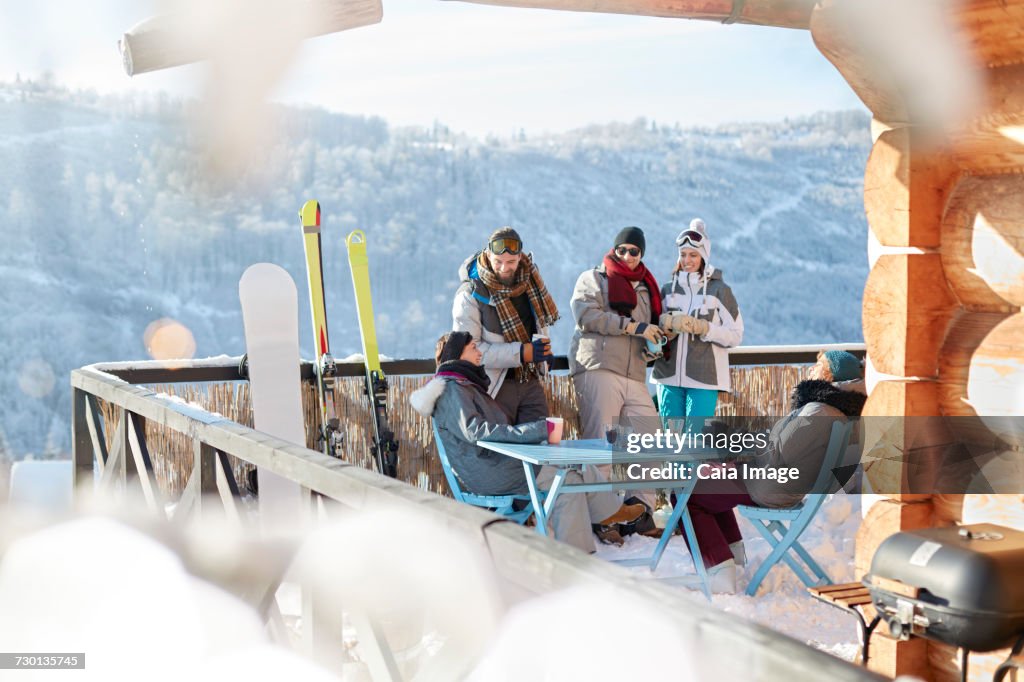 Skier and snowboarder couples hanging out on sunny cabin balcony apres-ski