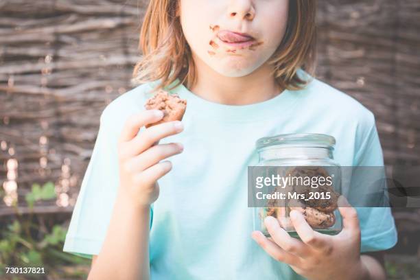 boy eating chocolate cookie while holding a jar of cookies  - child cookie jar stock-fotos und bilder