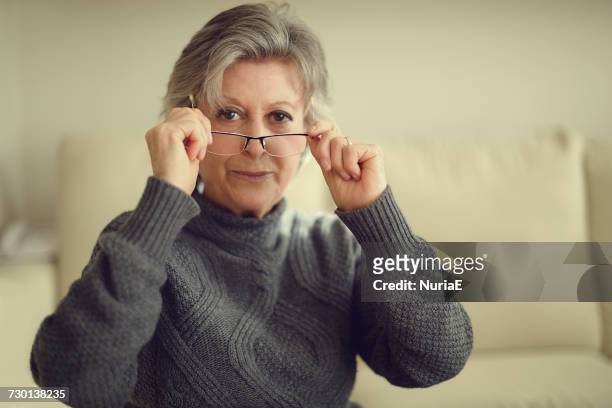 senior woman putting on her glasses - reading glasses 個照片及圖片檔