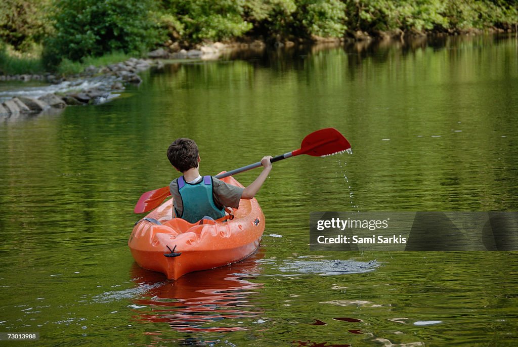 Boy (12-13) kayaking in river, rear view