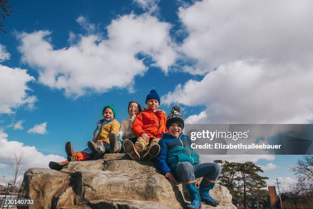 four children sitting on the top of a climbing rock at a playground  - front view portrait of four children sitting on rock stock pictures, royalty-free photos & images