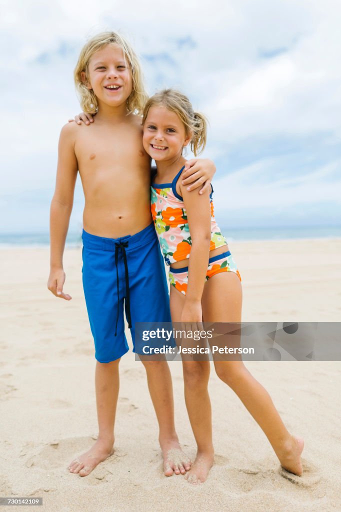 Brother (8-9) and sister (6-7) embracing on beach