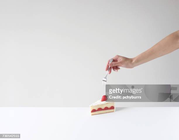 hand holding a fork about to eat a slice of cake - vork stockfoto's en -beelden